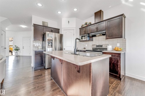 Kitchen featuring a central island with an integrated sink, dark wood-finish cabinetry, stainless steel appliances, and wood-finish flooring - 2292 Casey Crescent, Edmonton, AB - Indoor Photo Showing Kitchen With Double Sink With Upgraded Kitchen