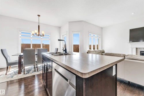 Open-concept living space featuring a central kitchen island with double sink, stainless steel dishwasher, and dark wood cabinetry - 2292 Casey Crescent, Edmonton, AB - Indoor With Fireplace