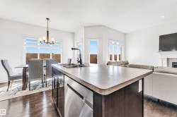 Open-concept living space featuring a central kitchen island with double sink, stainless steel dishwasher, and dark wood cabinetry - 