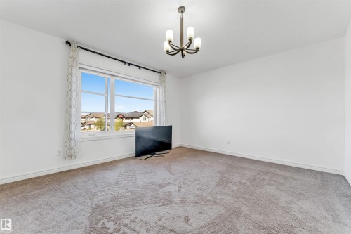 Bright interior space featuring a large picture window, neutral carpeting, white walls, and a multi-arm ceiling fixture - 2292 Casey Crescent, Edmonton, AB - Indoor Photo Showing Other Room