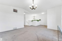 Spacious upper-level landing featuring neutral carpet flooring, white painted walls, and an overhead chandelier light fixture - 