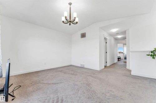 Open living area featuring neutral carpeting, a contemporary chandelier, and a hallway with recessed lighting - 2292 Casey Crescent, Edmonton, AB - Indoor Photo Showing Other Room