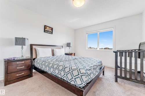 Carpeted room featuring a large window, a dark wood-finish bed frame with a light headboard, and a matching three-drawer nightstand - 2292 Casey Crescent, Edmonton, AB - Indoor Photo Showing Bedroom