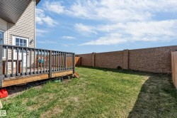 Spacious backyard with a raised wooden deck, a full stone privacy wall, and a wooden fence - 