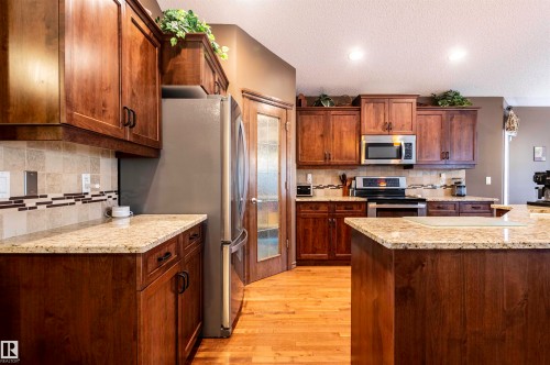 Kitchen featuring wood cabinetry, light-toned countertops, a tile backsplash with decorative accents, stainless steel appliances, and wood-finish flooring - 19 Newton Place, St. Albert, AB - Indoor Photo Showing Kitchen