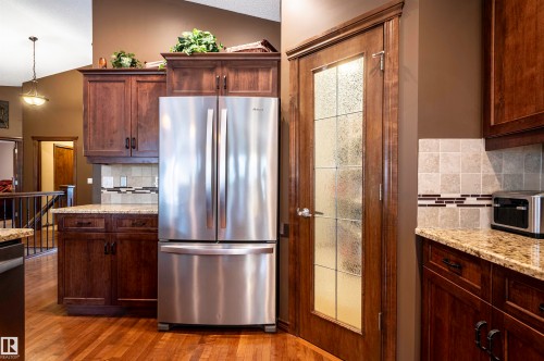 Kitchen featuring a stainless steel French door refrigerator, wood cabinetry, light granite countertops, and a decorative tile backsplash - 19 Newton Place, St. Albert, AB - Indoor Photo Showing Kitchen