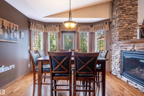 Dining area featuring a bay window, hardwood flooring, a stone-clad fireplace with a hearth, and a pendant light fixture - 19 Newton Place, St. Albert, AB - Indoor Photo Showing Dining Room With Fireplace