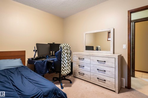 Carpeted room featuring a wood-finish headboard, a large wood-finish dresser with six drawers, a rectangular mirror, and a wood-trimmed doorway - 19 Newton Place, St. Albert, AB - Indoor Photo Showing Bedroom
