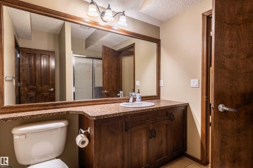 Bathroom featuring a vanity with a drop-in sink, granite-style countertop, dark wood-finish cabinetry, and an expansive framed mirror - 19 Newton Place, St. Albert, AB - Indoor Photo Showing Bathroom