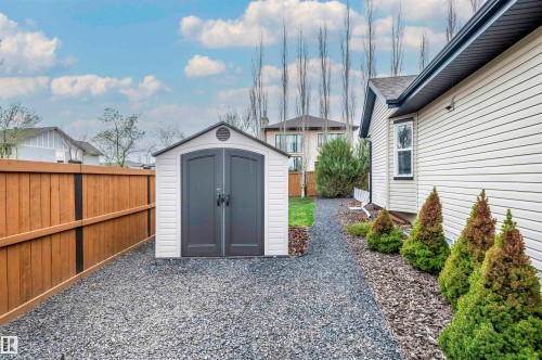 Gravel pathway featuring a freestanding shed with double doors, wood fencing, exterior siding, and foundation plantings - 19 Newton Place, St. Albert, AB - Outdoor