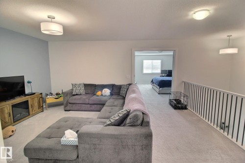 Spacious carpeted loft area featuring a partial accent wall, a built-in media console, and a contemporary railing system - 121 Stiles Bend, Leduc, AB - Indoor Photo Showing Living Room
