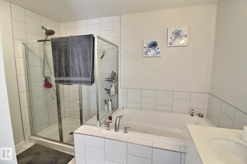 Bathroom featuring a built-in soaking tub, a glass-enclosed shower with subway tile surround, a single vanity with an integrated sink, and white tile wainscoting - 121 Stiles Bend, Leduc, AB - Indoor Photo Showing Bathroom