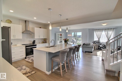 Open-concept main floor featuring wood-finish flooring, a contemporary kitchen island with a built-in sink, stainless steel appliances, and crisp white cabinetry - 121 Stiles Bend, Leduc, AB - Indoor Photo Showing Kitchen With Double Sink With Upgraded Kitchen