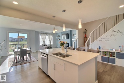 Open-concept kitchen featuring a large island with an undermount double sink, stainless steel appliances, pendant lighting, and wood-finish flooring - 121 Stiles Bend, Leduc, AB - Indoor Photo Showing Kitchen With Double Sink With Upgraded Kitchen