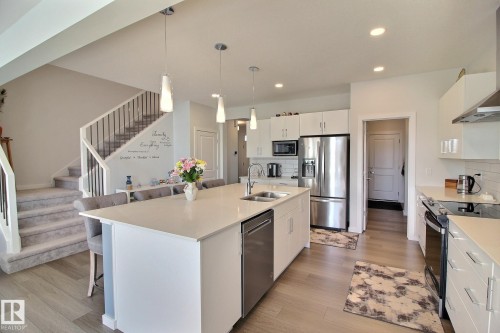Modern kitchen featuring a large central island with seating, white shaker cabinetry, stainless steel appliances, and light wood-finish flooring - 121 Stiles Bend, Leduc, AB - Indoor Photo Showing Kitchen With Double Sink With Upgraded Kitchen