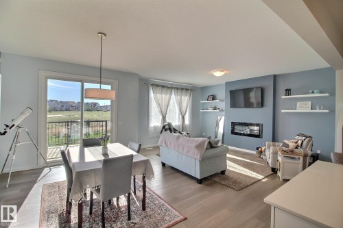 Open-concept living area featuring light wood-finish flooring, a built-in electric fireplace, and a sliding glass door leading to an outdoor balcony with metal railings - 121 Stiles Bend, Leduc, AB - Indoor With Fireplace