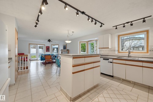 Kitchen featuring white cabinetry with wood-finish handles, light-toned tile flooring, granite-style countertops, and a stainless steel sink with a gooseneck faucet - 317 Hollick-Kenyon Road, Edmonton, AB - Indoor Photo Showing Kitchen