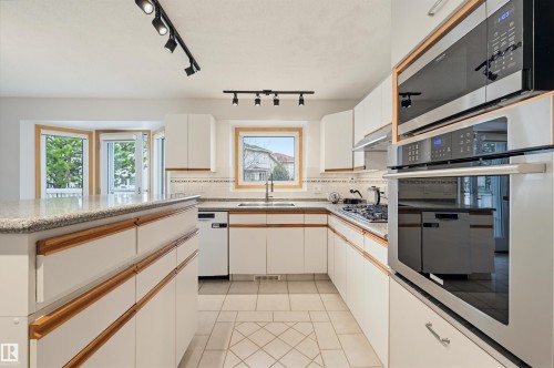 Kitchen featuring a large central island with a granite-style countertop, white cabinetry with wood trim, stainless steel appliances including a built-in oven and microwave, and track lighting fixtures - 317 Hollick-Kenyon Road, Edmonton, AB - Indoor Photo Showing Kitchen