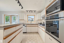 Kitchen featuring a large central island with a granite-style countertop, white cabinetry with wood trim, stainless steel appliances including a built-in oven and microwave, and track lighting fixtures - 