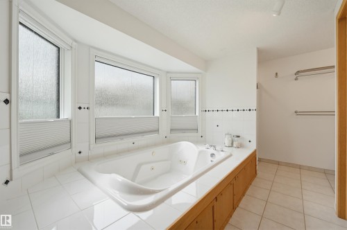 Corner jetted tub set within a tiled surround featuring multiple windows with privacy blinds - 317 Hollick-Kenyon Road, Edmonton, AB - Indoor Photo Showing Bathroom