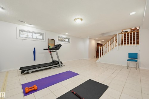 Spacious lower level featuring light-toned tile flooring, recessed lighting, and a prominent wood staircase with white balusters - 317 Hollick-Kenyon Road, Edmonton, AB - Indoor Photo Showing Gym Room