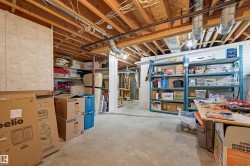 Unfinished basement featuring exposed wood joists, concrete flooring, and extensive storage shelving - 