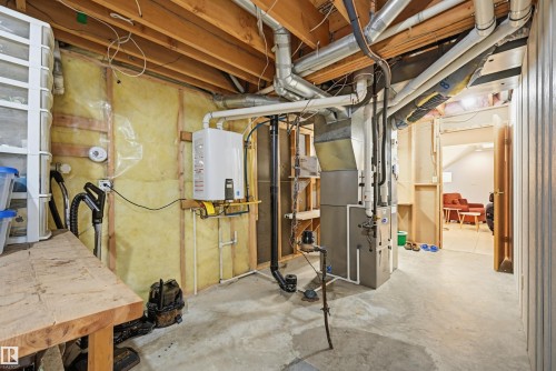 Basement utility area featuring a tankless water heater, furnace, exposed ceiling joists, and concrete flooring - 317 Hollick-Kenyon Road, Edmonton, AB - Indoor Photo Showing Basement
