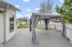 Expansive exterior deck featuring a grey finish, white railings, a bay window, and a grey gazebo - 