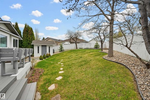 Spacious yard featuring a sloped lawn, stone paver path, white privacy fencing, and a detached white storage shed with a dark gray door and trim - 317 Hollick-Kenyon Road, Edmonton, AB - Outdoor