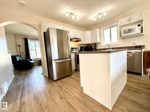 Kitchen featuring stainless steel appliances, white cabinetry, dark countertops, and an island with a sink - 645 Windross Crescent, Edmonton, AB 