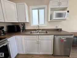 Kitchen featuring white cabinetry, a double basin stainless steel sink, a stainless steel dishwasher, and wood-finish flooring - 