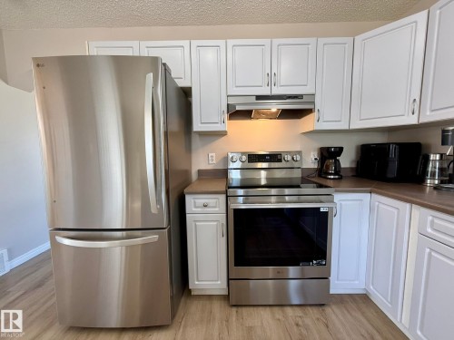 Kitchen featuring stainless steel appliances, white cabinetry with silver-tone hardware, and wood-finish flooring - 645 Windross Crescent, Edmonton, AB 