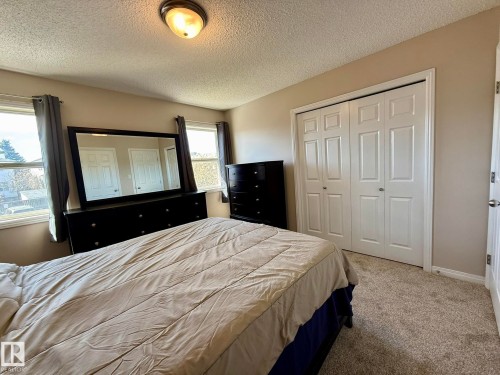 Carpeted bedroom featuring two windows with window treatments, a flush-mount ceiling light fixture, and bi-fold closet doors - 645 Windross Crescent, Edmonton, AB 