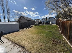 Expansive backyard featuring a sloped lawn, wood fencing, concrete patio area, and a white storage shed - 