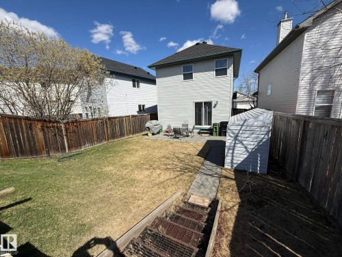 Landscaped backyard featuring a paved patio area, rear house entrance with sliding glass doors, a storage shed, and perimeter fencing - 645 Windross Crescent, Edmonton, AB 