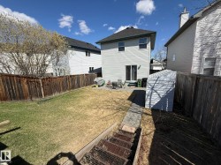 Landscaped backyard featuring a paved patio area, rear house entrance with sliding glass doors, a storage shed, and perimeter fencing - 