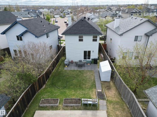 Rear exterior featuring a patio with pavers, a grass lawn, two raised garden beds, and a storage shed - 645 Windross Crescent, Edmonton, AB 