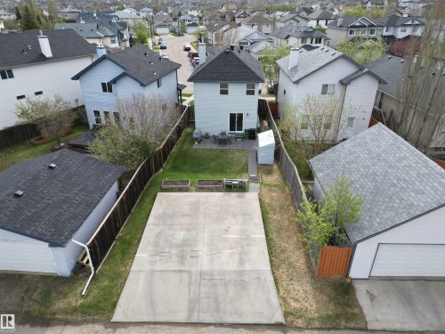 Expansive concrete pad and fenced backyard featuring a patio area, mature trees, and raised garden beds - 645 Windross Crescent, Edmonton, AB 