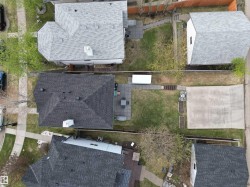 Aerial perspective showcasing a property with a dark shingle roof, a paved patio area, and a large concrete pad - 