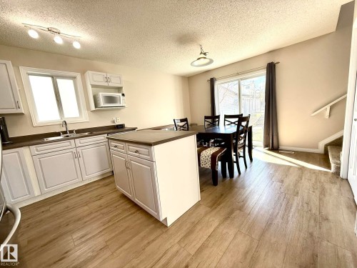 Open-concept kitchen and dining area featuring white cabinetry, dark countertops, a central island, wood-finish flooring, and a sliding glass door to the exterior - 645 Windross Crescent, Edmonton, AB 
