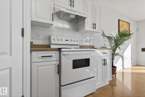 Kitchen featuring white shaker-style cabinetry with matte black hardware, white tile backsplash, and a white electric range with matching range hood - 421 84 Street, Edmonton, AB - Indoor Photo Showing Kitchen