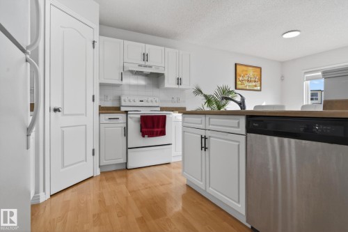 Modern kitchen featuring white cabinetry with dark hardware, a stainless steel dishwasher, wood-finish flooring, light countertops, and a white tile backsplash - 421 84 Street, Edmonton, AB - Indoor Photo Showing Kitchen