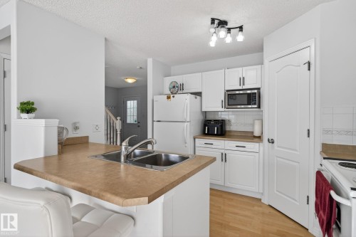 Kitchen featuring white cabinetry, a double basin stainless steel sink, a built-in microwave, light wood-finish flooring, and track lighting - 421 84 Street, Edmonton, AB - Indoor Photo Showing Kitchen With Double Sink