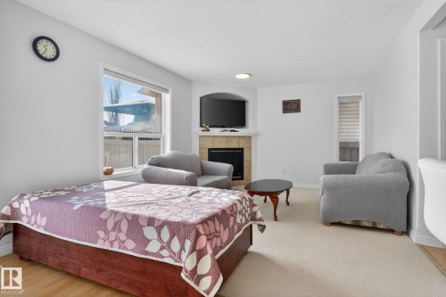 Living area featuring a corner fireplace with a tile surround and mantel, a large window, and light-toned carpeting - 421 84 Street, Edmonton, AB - Indoor Photo Showing Bedroom