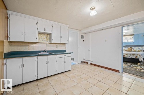 Kitchen area featuring extensive white cabinetry, a teal countertop, and a stainless steel sink with a dual-handle faucet - 10939 96 Street, Edmonton, AB - Indoor Photo Showing Kitchen