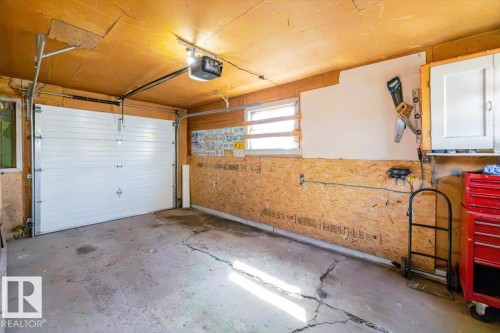 Single-car garage featuring a white overhead door with an automatic opener, exposed wood-finish ceiling, and oriented strand board walls - 10939 96 Street, Edmonton, AB - Indoor Photo Showing Garage