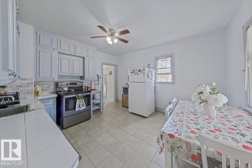 Bright kitchen featuring white cabinetry, light tile flooring, stainless steel range, light-toned countertops, and a ceiling fan - 10939 96 Street, Edmonton, AB - Indoor Photo Showing Kitchen