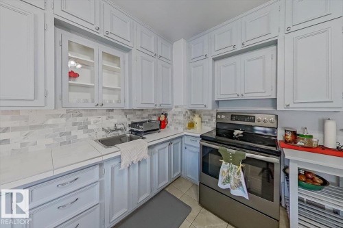 Kitchen featuring light-toned cabinetry with metal hardware, a subway tile backsplash, and a stainless steel electric range - 10939 96 Street, Edmonton, AB - Indoor Photo Showing Kitchen