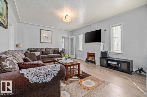 Light-filled living area featuring wood-finish flooring, a white-painted brick fireplace, and built-in crown molding - 10939 96 Street, Edmonton, AB - Indoor Photo Showing Living Room
