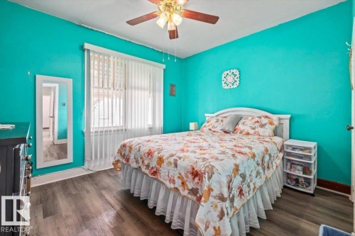 Bedroom featuring wood-finish flooring, a ceiling fan with integrated lighting, and a large window with vertical blinds - 10939 96 Street, Edmonton, AB - Indoor Photo Showing Bedroom